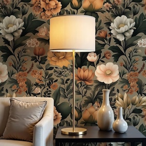 May include: A floor lamp with a cream-colored lampshade and a gold-colored base stands next to a black table. Two white vases are on the table. The background is a floral wallpaper with large flowers in shades of peach, white, and green.