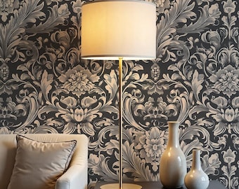 May include: A floor lamp with a beige lampshade and a gold-colored base and pole stands next to a black table. Two small, light-colored vases are on the table. The background is a dark wallpaper with a floral pattern.