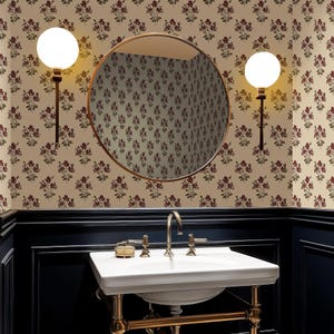 May include: A bathroom scene featuring a white sink with gold fixtures, a round mirror, and two globe lights. The walls are covered in floral wallpaper, and the lower portion is painted navy blue.