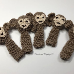 May include: Five handmade crochet monkey toys. Each monkey has a brown body, beige face, and small ears. The toys are arranged on a white surface. The text "Carolann Crafting" is visible.