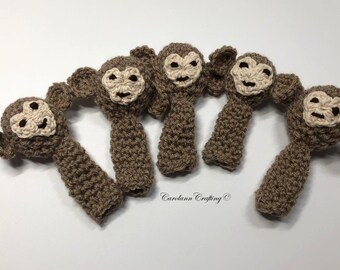May include: Five handmade crochet monkey toys. Each monkey has a brown body, tan face, and small ears. The toys are arranged on a white surface. The text "Carolann Crafting" is visible.