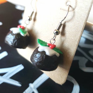 May include: A pair of silver dangle earrings with a miniature Christmas pudding charm. The pudding is brown with white icing and green holly leaves with red berries.