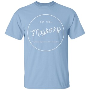 May include: Light blue t-shirt with a white circle graphic that says "Mayberry" in a cursive font. The circle also says "EST. 1864" and "Founded by James Merriweather".