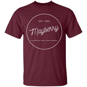 May include: Burgundy t-shirt with a white circle graphic that says "Mayberry" in a cursive font. The circle also includes the text "EST. 1864" and "Founded by James Merriweather".