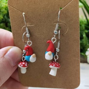 May include: A pair of silver dangle earrings with red and white mushroom charms and blue and red gnome charms.
