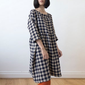 Può includere: Un abito al ginocchio con motivo a quadri blu navy e beige. L'abito ha uno scollo tondo e maniche a tre quarti. La modella indossa leggings arancioni.