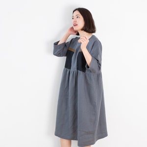 Könnte beinhalten: Ein graues Leinenkleid mit schwarzen und braunen geometrischen Paneelen. Das Kleid hat eine lockere Passform und einen leicht gerafften Rock.