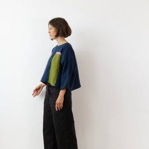 Könnte beinhalten: Eine Frau trägt ein locker sitzendes, marineblaues Leinenoberteil mit einem geometrischen Muster in Grün, Rosa und Weiß. Sie trägt eine schwarze Hose.