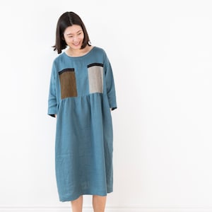 Könnte beinhalten: Eine Frau trägt ein blaues Leinenkleid mit Patchwork-Muster in Braun, Schwarz und Weiß. Das Kleid hat einen gerafften Rock und Dreiviertelärmel.