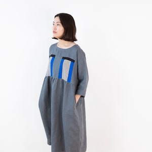 Könnte beinhalten: Ein graues Leinenkleid mit einem blauen und schwarzen geometrischen Muster auf dem Oberteil. Das Kleid hat eine lockere Passform und einen leicht gerafften Rock.