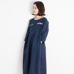 Könnte beinhalten: Ein marineblaues Leinenkleid mit einem pinkfarbenen und grünen Streifen-Detail. Das Kleid hat einen runden Ausschnitt und Dreiviertelärmel.