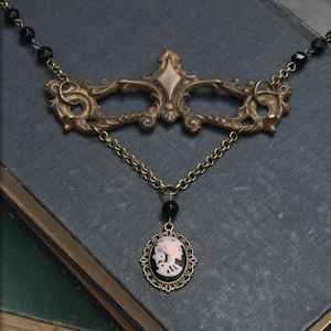 May include: A black and gold necklace with a cameo pendant. The cameo features a white profile of a woman. The necklace is made with black beads and a gold chain.