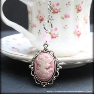 May include: A silver tea infuser with a pink cameo charm featuring a woman's profile. The infuser is hanging from a silver chain with a pink bead.