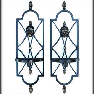 May include: Pair of black metal wall sconces with a skull design. Each sconce features a decorative frame with a skull in the center, a candle holder, and ornate detailing. The sconces are designed for wall mounting and add a gothic touch.