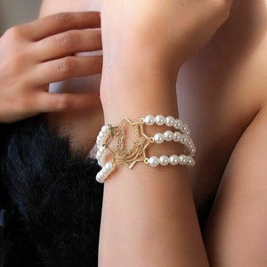 May include: A gold bracelet with a star-shaped charm and three rows of white pearls.