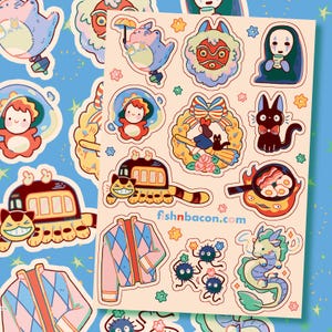 May include: A sheet of colourful stickers featuring various cartoon characters and designs. The stickers include a train with a smiling face, a dragon, a cat with a bow tie, and a character with a mask. The website fishnbacon.com is printed on the sheet.