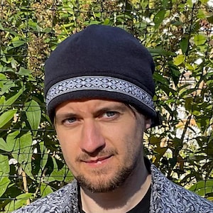 May include: A black fleece beanie with a white and black geometric patterned band around the crown.