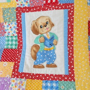 May include: A patchwork quilt with a central square featuring a cartoon puppy reading a book titled "Puppy Welcomes". The quilt has a variety of colorful patterned squares, including floral, polka dot, and gingham designs.