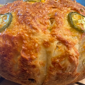 May include: A golden brown bread loaf with a cheesy crust and green jalapeno pepper slices on top.