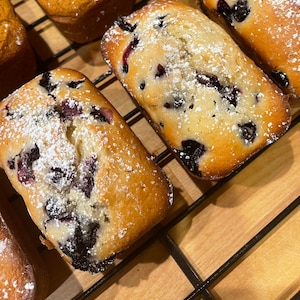 May include: Close-up of blueberry muffins with powdered sugar on top. The muffins are on a wire rack.