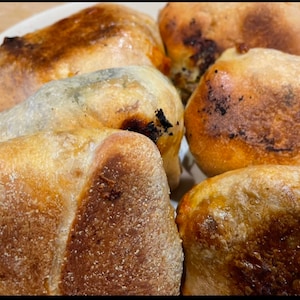 May include: Close-up of five golden brown, baked bread pockets. The pockets are slightly puffed and have a slightly crispy texture.