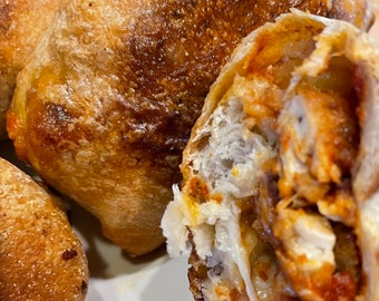 May include: Close-up of a baked bread roll with a cheesy, meaty filling. The bread is golden brown and the filling is visible through a tear in the bread.