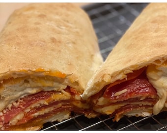 May include: A close-up of a pizza roll cut in half, revealing layers of pepperoni, cheese, and sauce inside a golden brown dough.