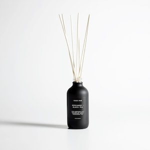 May include: A black diffuser bottle with white reeds. The bottle has a matte finish and a label that reads "TRUE HUE BERGAMOT + BLACK TEA." The reeds are thin and light-colored, extending upwards from the bottle's opening. The product is set against a white background.