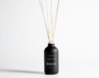 Może przedstawiać: Czarny flakon z dyfuzorem z białym napisem "TRUE HUE" i "FOREST FERN". Butelka zawiera kilka białych patyczków. Produkt przeznaczony do aromaterapii i zapachu w domu.