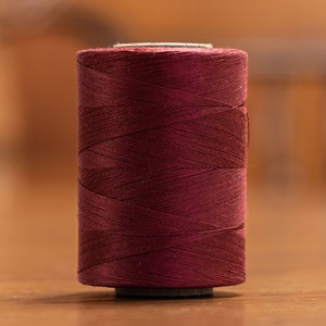 May include: A spool of deep burgundy red thread.