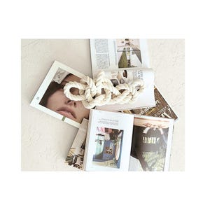 May include: A thick, white rope tied in a decorative knot. The rope is displayed on top of several open magazines.