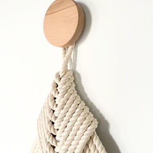 May include: A white cotton rope wall hanging with a knotted design, attached to a round wooden knob.