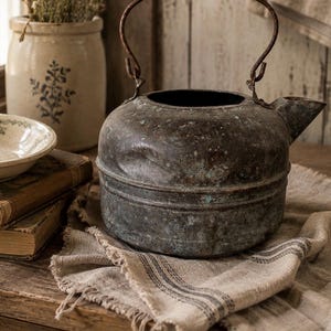 May include: A weathered, dark metal kettle with a rounded body, a prominent spout, and a thin, arched wire handle. The surface shows significant oxidation, featuring mottled brown and teal-green patina with visible dents and a textured finish.