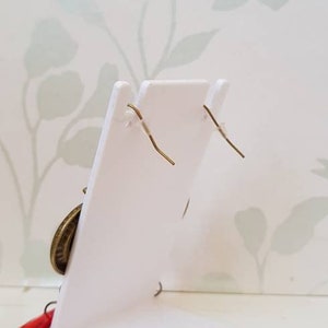 May include: A pair of earrings with a gold-toned metal design and red glass accents. The earrings are displayed on a white stand against a floral background.