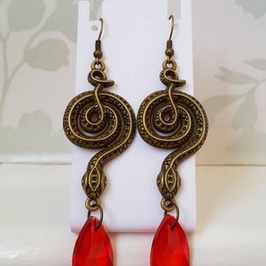 May include: A pair of gold-tone snake dangle earrings with red crystal drops. The snake is coiled and has a textured surface.