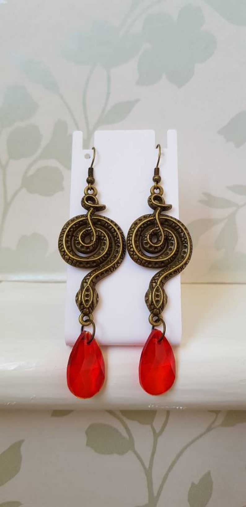 May include: A pair of gold-tone snake dangle earrings with red crystal drops. The snake is coiled and has a textured surface.