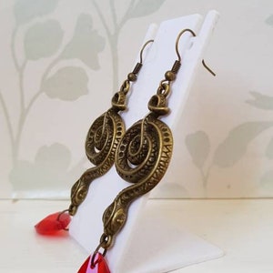 May include: A pair of gold-tone snake earrings with red teardrop-shaped crystal accents.