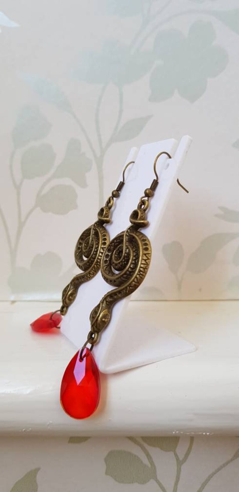 May include: A pair of gold-tone snake earrings with red teardrop-shaped crystal accents.