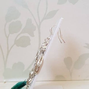 May include: Silver dangle earrings with a detailed design and emerald green teardrop crystals.