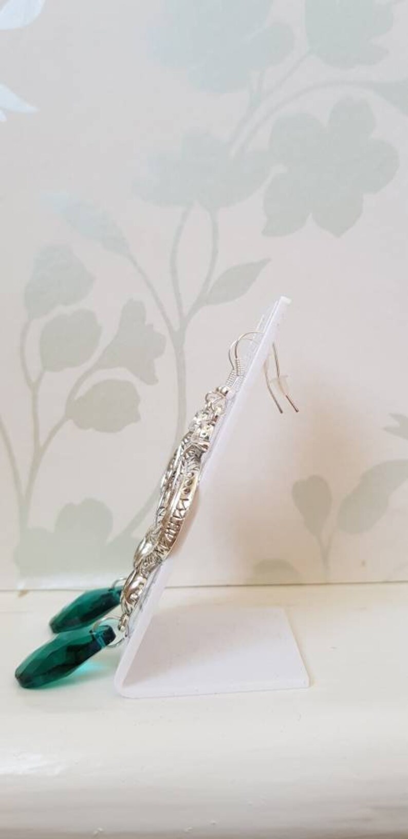 May include: Silver dangle earrings with a detailed design and emerald green teardrop crystals.