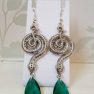 May include: Silver snake earrings with green teardrop-shaped crystal accents.