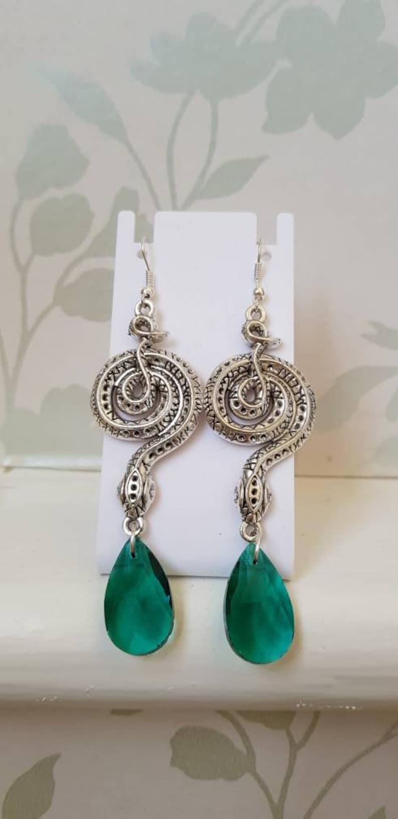 May include: Silver snake earrings with green teardrop-shaped crystal accents.
