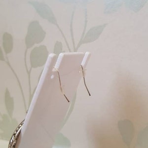 May include: A pair of silver earrings with a circular design. The earrings are on a white display stand.