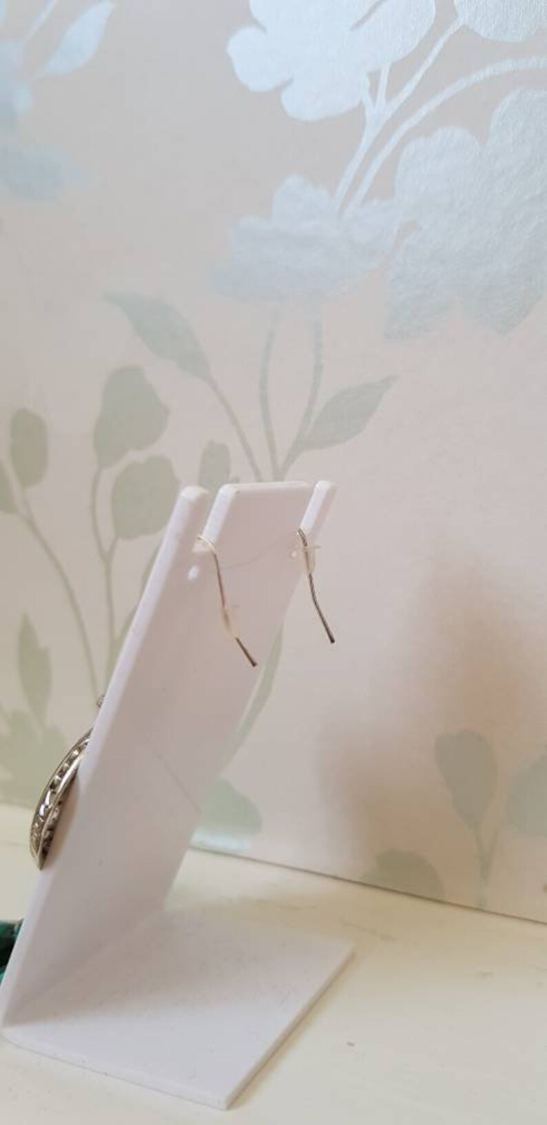 May include: A pair of silver earrings with a circular design. The earrings are on a white display stand.