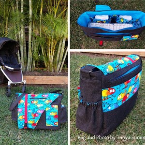 Op de afbeelding: Een zwarte luiertas met een kleurrijke kameleonprint. De tas heeft een groot hoofdvak, een ritsvak en een kleiner vak aan de voorkant. De tas wordt getoond met een kinderwagen op de achtergrond.