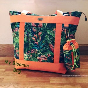 Pu&ograve; includere: Una grande borsa tote con una stampa floreale tropicale, con foglie verdi e fiori rosa, accentuata da finiture e cinghie arancioni. Include una pochette con coulisse abbinata. Il testo "My Bloomin' Bag" &egrave; visibile.