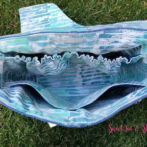 Op de afbeelding: Binnenkant van een blauwe en witte geprinte tote bag met meerdere vakken. De tas heeft een blauwe en witte gestreepte voering en een blauwe elastische band aan de bovenkant.