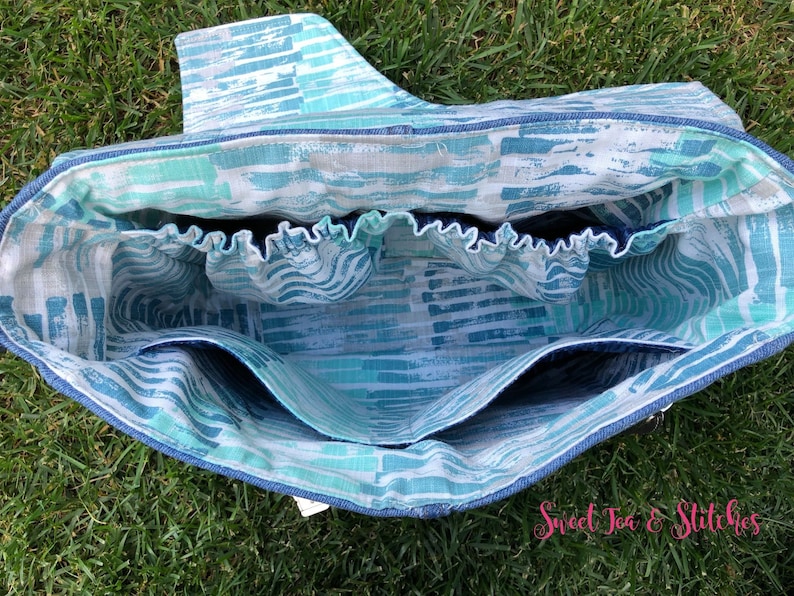 Op de afbeelding: Binnenkant van een blauwe en witte geprinte tote bag met meerdere vakken. De tas heeft een blauwe en witte gestreepte voering en een blauwe elastische band aan de bovenkant.