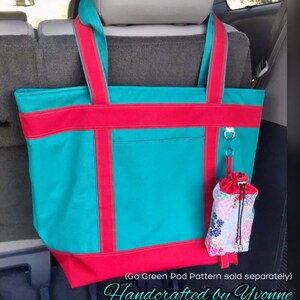 Pu&ograve; includere: Una grande borsa tote turchese con finiture e manici rossi. Un piccolo astuccio con stampa floreale &egrave; appeso a un anello di metallo attaccato alla borsa. Il testo "Handcrafted by Yvonne" &egrave; in basso.