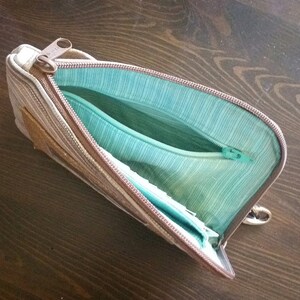 Pode incluir: Uma bolsa com z&iacute;per de listras marrons e bege com um forro turquesa. A bolsa est&aacute; aberta e o z&iacute;per &eacute; vis&iacute;vel.